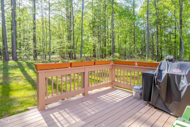 wooden terrace with a view of trees, a lawn, and area for grilling