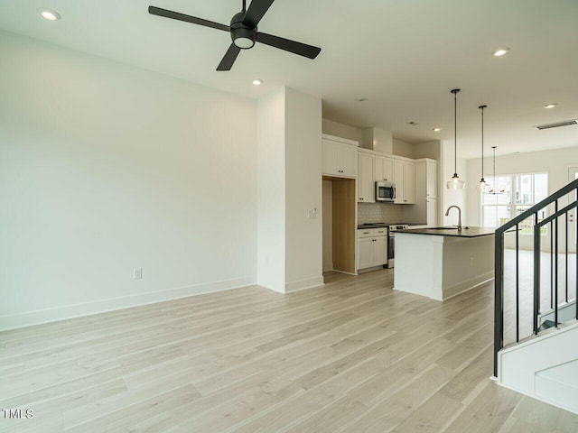 interior space featuring appliances with stainless steel finishes, tasteful backsplash, an island with sink, white cabinetry, and ceiling fan