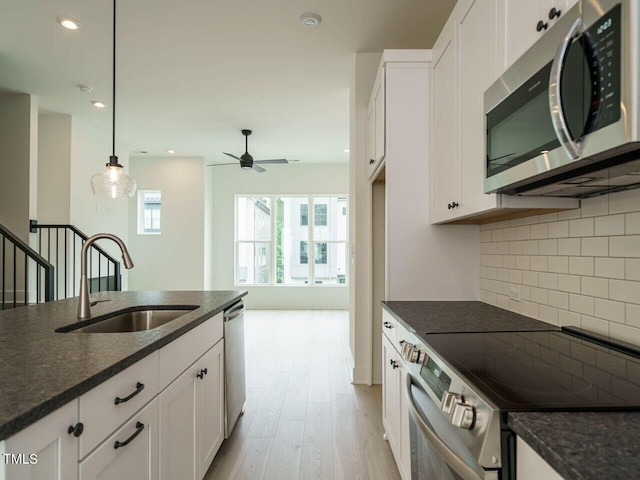 kitchen with light wood-type flooring, backsplash, stainless steel appliances, hanging light fixtures, and sink