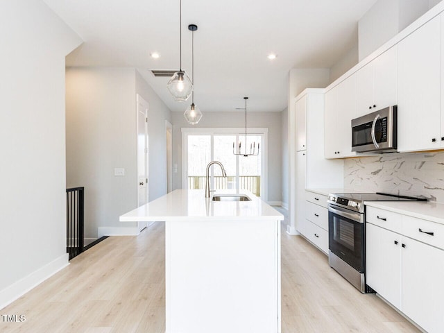 kitchen with tasteful backsplash, a kitchen island with sink, stainless steel appliances, light wood-type flooring, and a sink