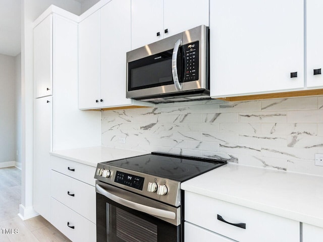 kitchen featuring stainless steel appliances, white cabinets, light countertops, light wood-type flooring, and decorative backsplash