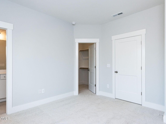 unfurnished bedroom featuring a walk in closet, baseboards, visible vents, and carpet flooring