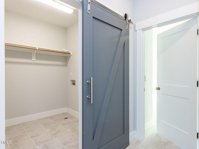 clothes washing area featuring laundry area, a barn door, hookup for a washing machine, and baseboards