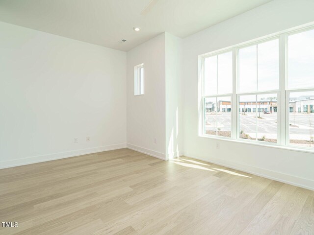 empty room featuring light wood finished floors, visible vents, and baseboards