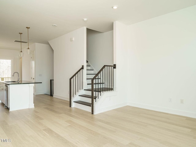 interior space featuring light wood-style floors, a sink, stairway, and baseboards