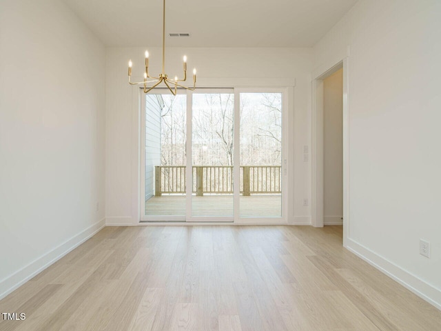 unfurnished room featuring baseboards, visible vents, light wood-style flooring, and a notable chandelier