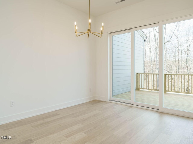 spare room featuring light wood-style floors, a chandelier, visible vents, and baseboards