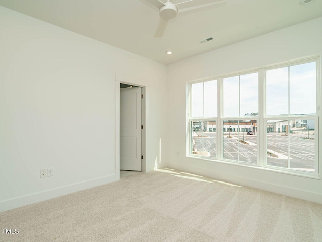 carpeted spare room featuring a healthy amount of sunlight, baseboards, visible vents, and a ceiling fan