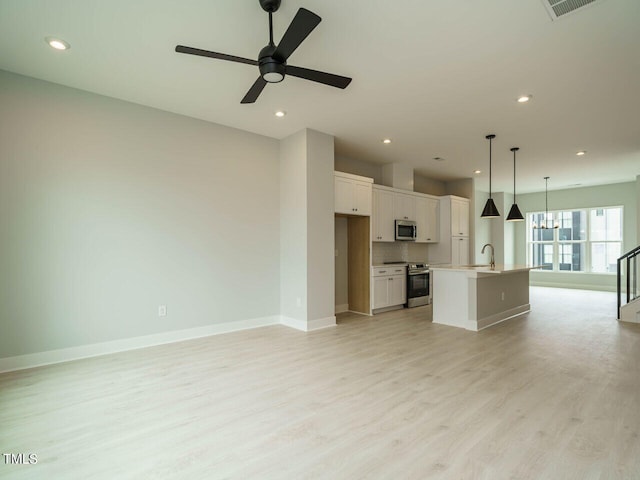 unfurnished living room featuring light wood-style flooring, recessed lighting, ceiling fan with notable chandelier, a sink, and baseboards