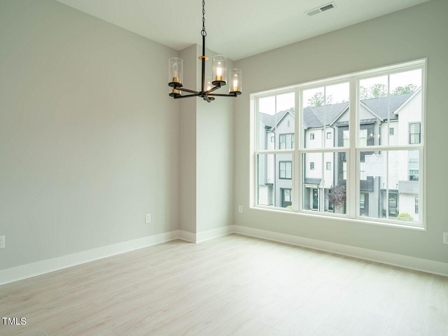 unfurnished room featuring an inviting chandelier, baseboards, visible vents, and light wood-style floors