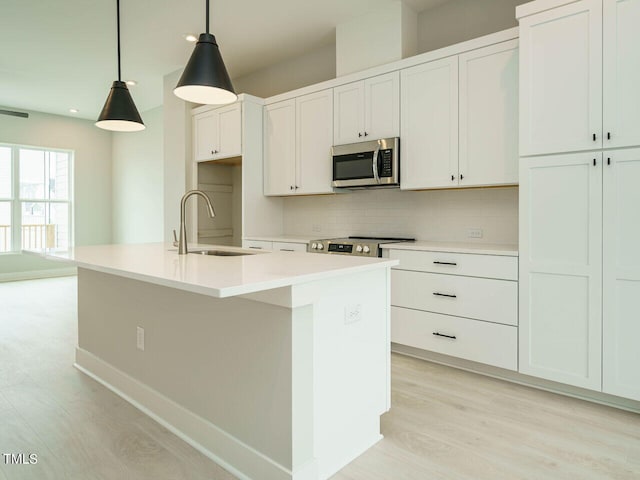 kitchen with a kitchen island with sink, a sink, appliances with stainless steel finishes, light wood-type flooring, and decorative backsplash