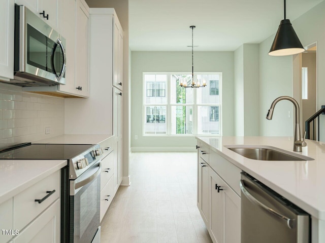 kitchen featuring a sink, white cabinets, appliances with stainless steel finishes, tasteful backsplash, and decorative light fixtures