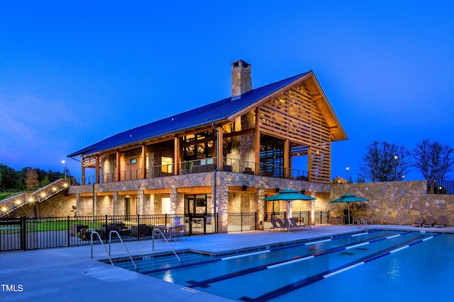 exterior space featuring a balcony, stone siding, a community pool, fence, and a patio area