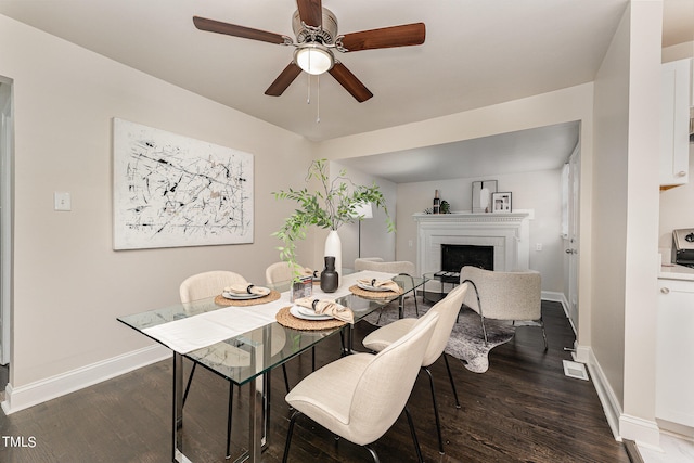 dining area featuring ceiling fan, a fireplace, and dark hardwood / wood-style flooring