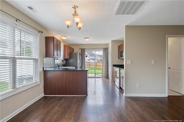 kitchen featuring decorative light fixtures, dark hardwood / wood-style flooring, kitchen peninsula, stainless steel appliances, and decorative backsplash