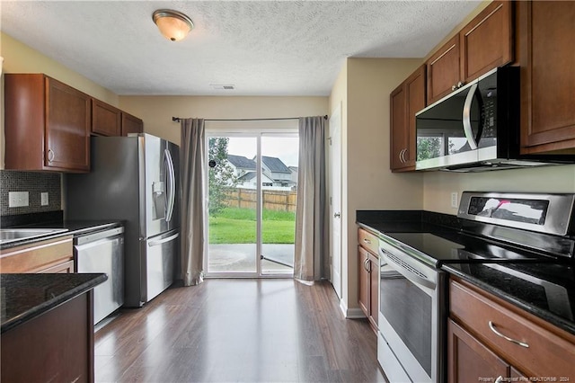 kitchen with appliances with stainless steel finishes, dark hardwood / wood-style flooring, and dark stone counters