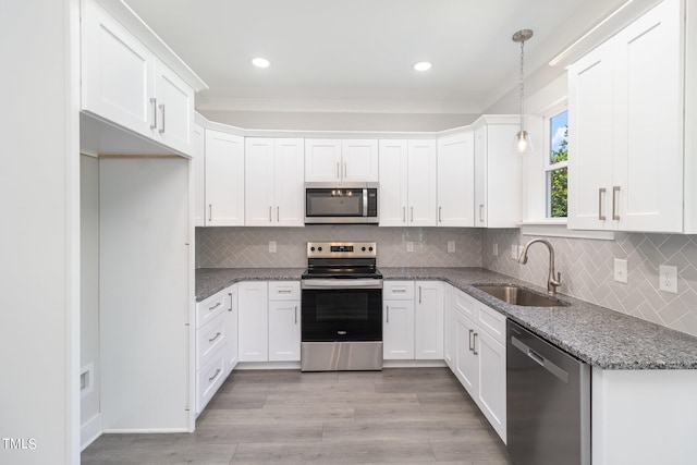 kitchen with sink, hanging light fixtures, appliances with stainless steel finishes, dark stone counters, and white cabinets