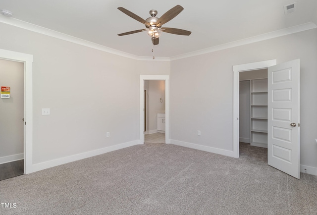 unfurnished bedroom featuring a walk in closet, light colored carpet, ceiling fan, crown molding, and a closet