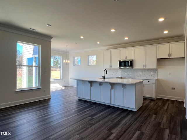 kitchen featuring sink, a center island with sink, ornamental molding, white cabinets, and backsplash