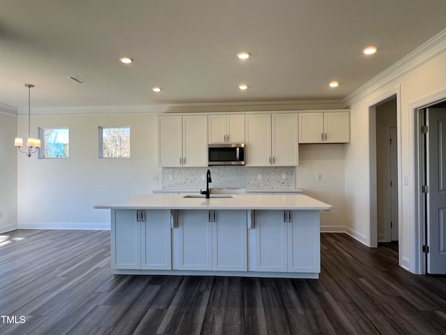 kitchen featuring decorative light fixtures, ornamental molding, an island with sink, and white cabinets