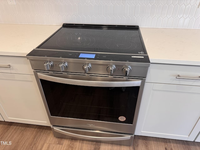 room details featuring white cabinetry, hardwood / wood-style floors, and stainless steel range with electric stovetop