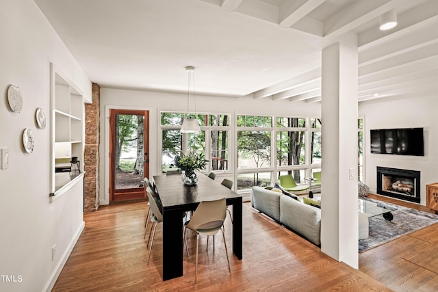 dining room featuring beam ceiling, baseboards, a fireplace, and wood finished floors