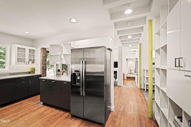 kitchen featuring light countertops, open shelves, light wood-type flooring, dark cabinetry, and stainless steel fridge with ice dispenser