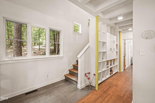 stairway featuring baseboards, a healthy amount of sunlight, beamed ceiling, and visible vents