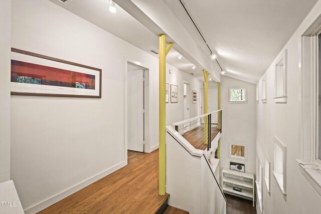 hallway with track lighting, hardwood / wood-style flooring, and vaulted ceiling