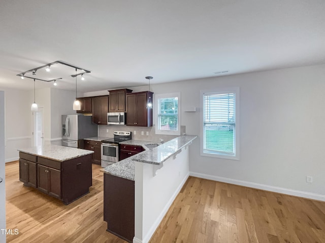 kitchen with light stone counters, hanging light fixtures, light hardwood / wood-style flooring, and stainless steel appliances