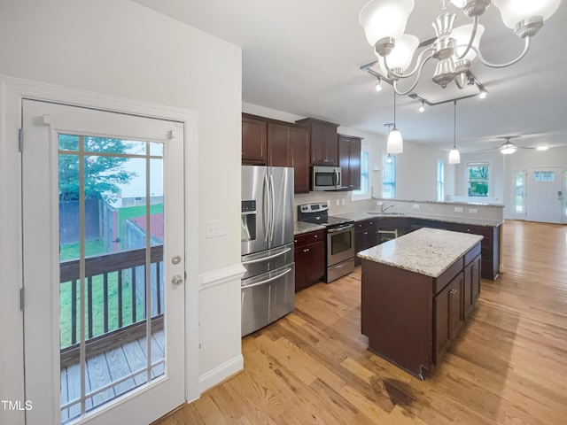 kitchen with pendant lighting, light hardwood / wood-style flooring, appliances with stainless steel finishes, light stone countertops, and a kitchen island