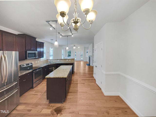 kitchen with light hardwood / wood-style flooring, appliances with stainless steel finishes, hanging light fixtures, light stone countertops, and a kitchen island