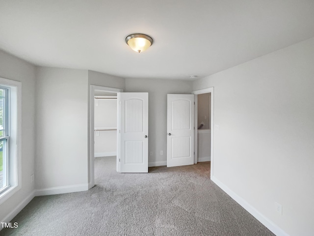 unfurnished bedroom with a walk in closet, a closet, and light carpet