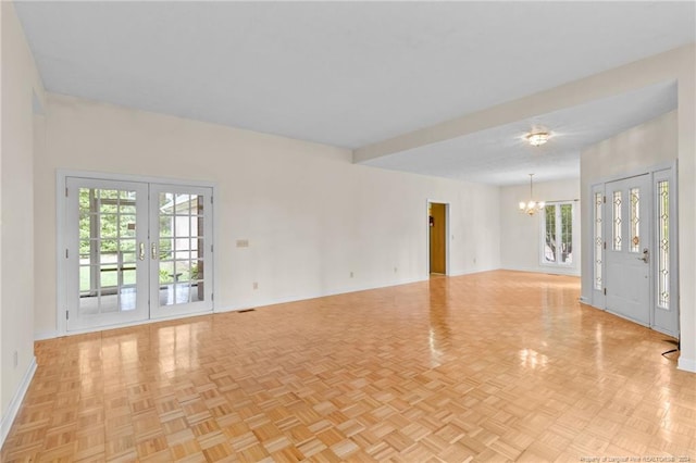 unfurnished room featuring french doors, a notable chandelier, plenty of natural light, and light parquet floors