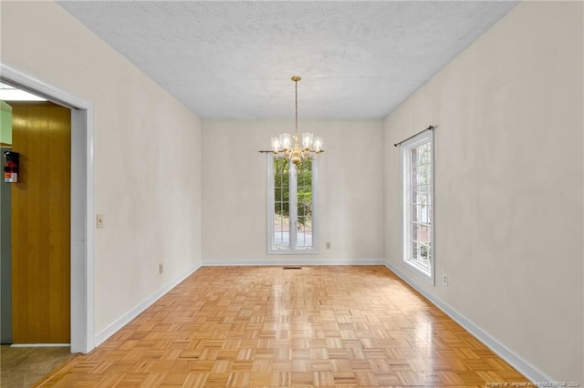 spare room with a textured ceiling, a notable chandelier, and light parquet floors