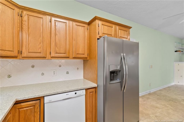 kitchen with stainless steel fridge, light stone counters, white dishwasher, and backsplash