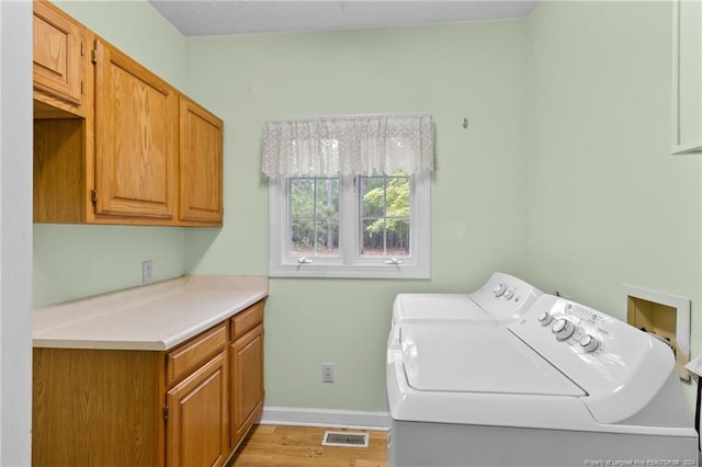 laundry area featuring independent washer and dryer, light hardwood / wood-style floors, and cabinets