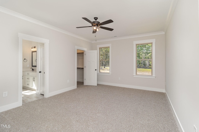 unfurnished bedroom featuring crown molding, ceiling fan, ensuite bathroom, a walk in closet, and light colored carpet