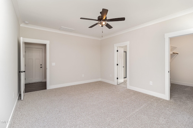 unfurnished bedroom featuring crown molding, light colored carpet, ceiling fan, and a walk in closet