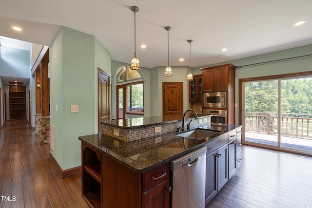 kitchen with decorative backsplash, stainless steel appliances, sink, decorative light fixtures, and an island with sink