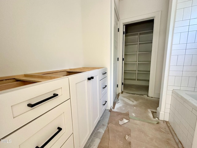 full bathroom with a walk in closet and a relaxing tiled tub