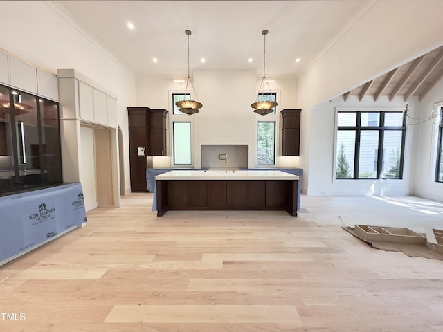 7208 Tanbark Way, Raleigh, NC 27615 - kitchen featuring light countertops, an island with sink, dark brown cabinets, light wood-type flooring, and decorative light fixtures