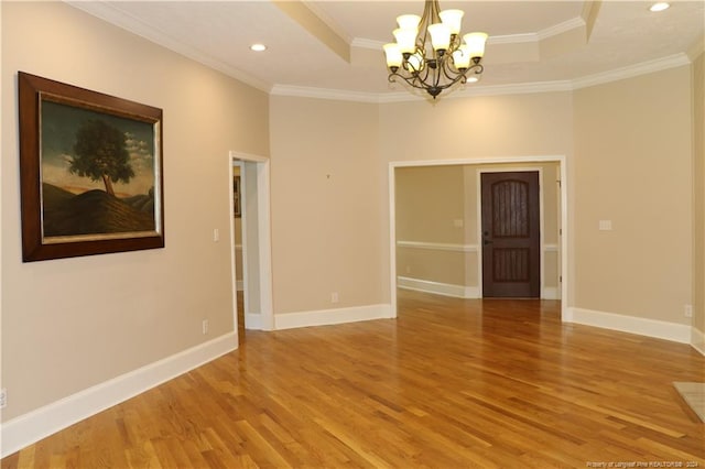 spare room featuring crown molding, an inviting chandelier, light hardwood / wood-style floors, and a tray ceiling