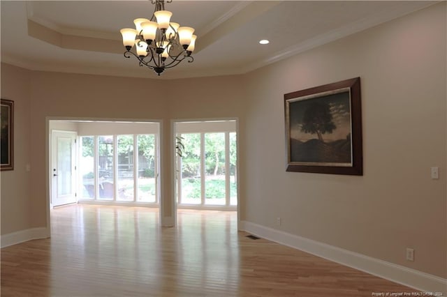 unfurnished room with hardwood / wood-style floors, a raised ceiling, a chandelier, and ornamental molding