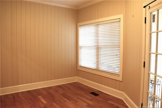 empty room featuring a wealth of natural light, ornamental molding, and hardwood / wood-style flooring