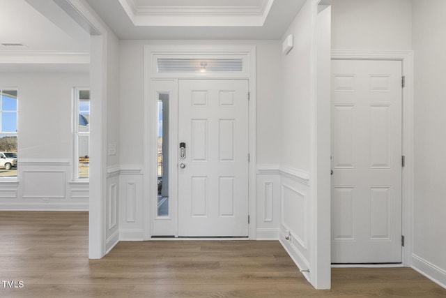 foyer entrance featuring a raised ceiling, light wood-type flooring, and ornamental molding