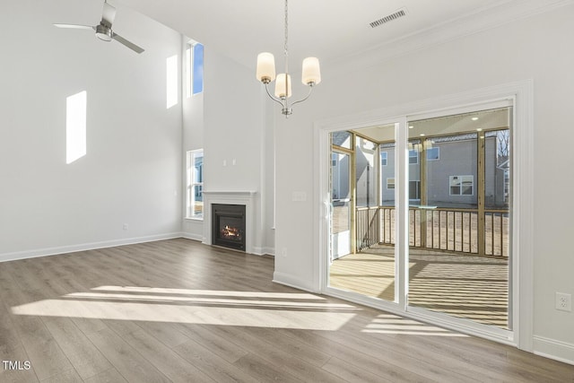 unfurnished living room with crown molding, ceiling fan with notable chandelier, and hardwood / wood-style flooring