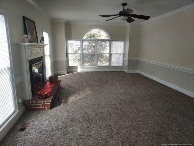 unfurnished living room featuring carpet flooring, ornamental molding, ceiling fan, a brick fireplace, and plenty of natural light