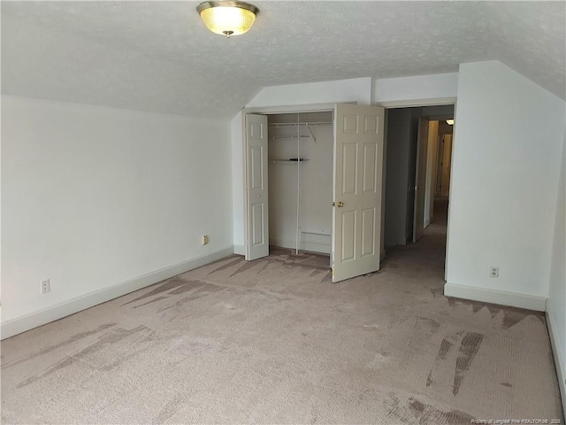 unfurnished bedroom with a closet, a textured ceiling, light carpet, and vaulted ceiling