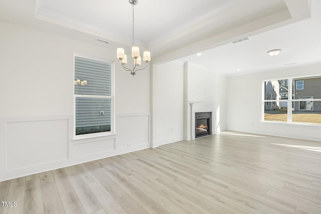 unfurnished living room featuring light hardwood / wood-style flooring, an inviting chandelier, and a raised ceiling